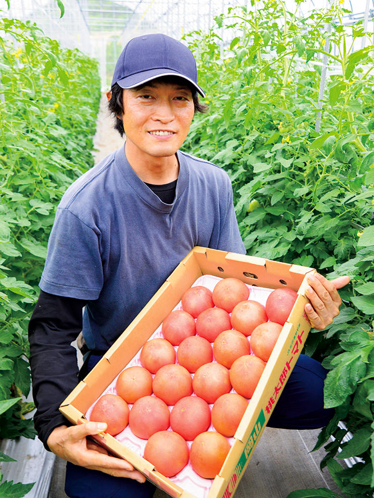 箱詰めしたトマトを持って笑顔の原さんの写真