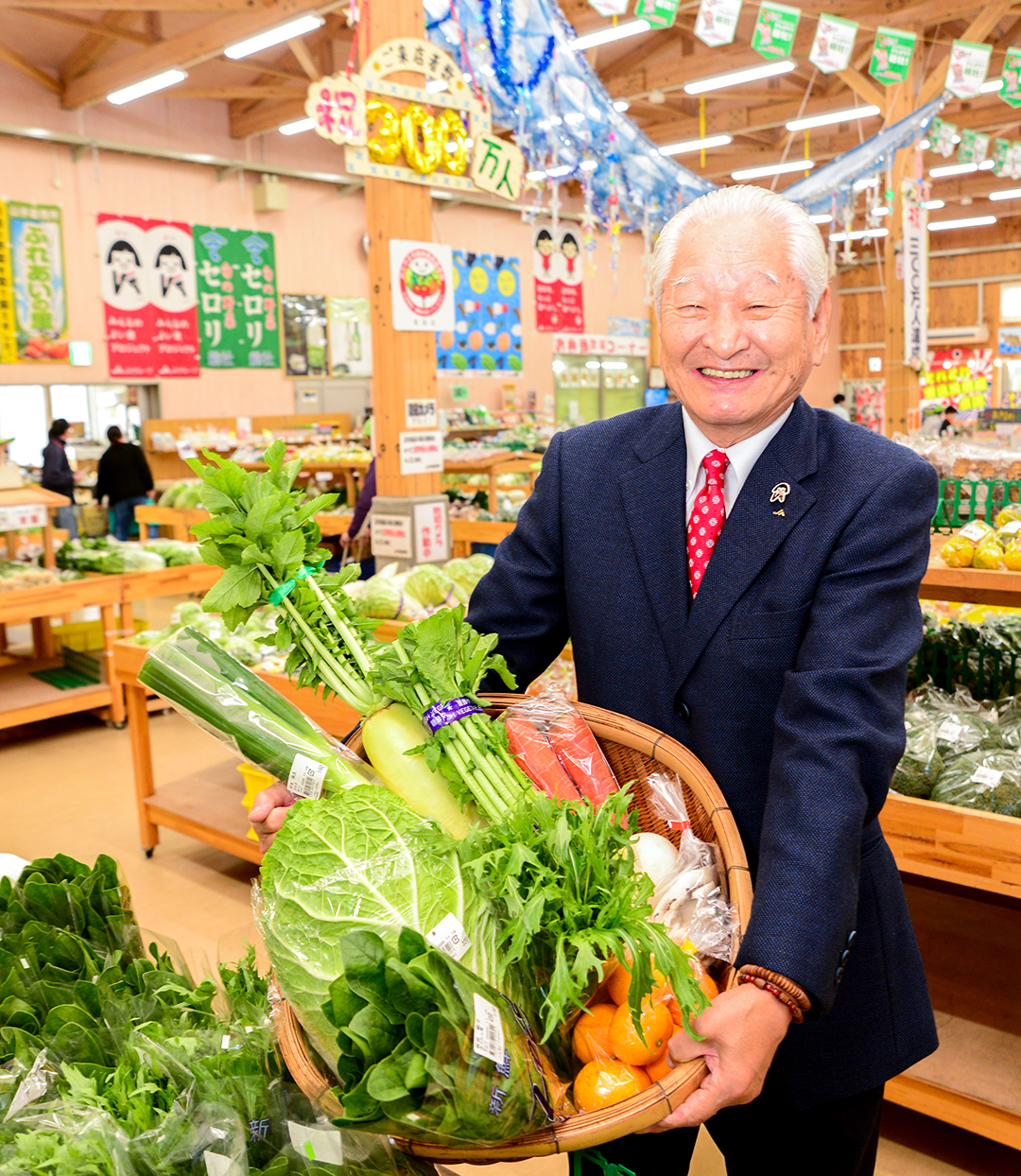 野菜のカゴ盛りを抱えた笑顔の石我組合長の写真