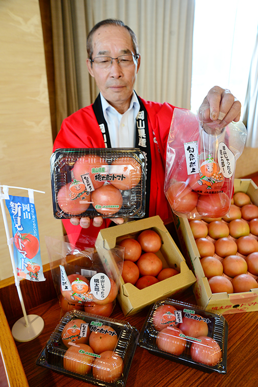 手提げ袋やパック詰め商品をPRする橋本部会長の写真