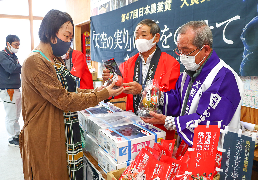 観光客に試食用の「天空の実り」シリーズを渡す藤井部会長（手前）と仲山部会長の写真