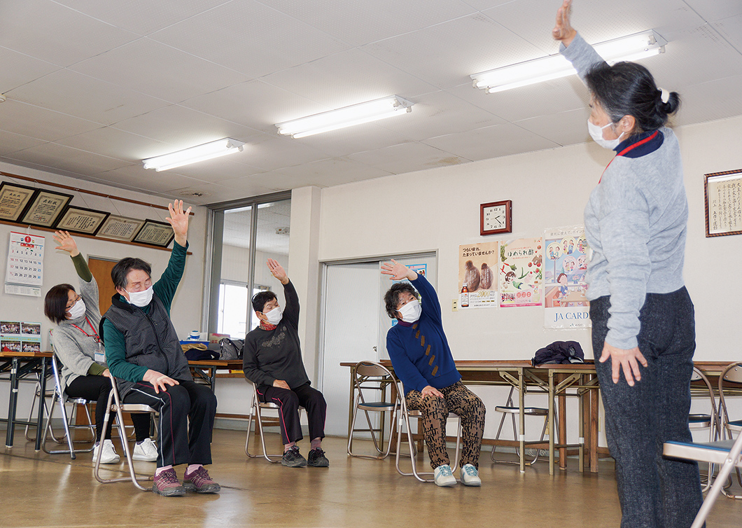 保健師(右)の指導で、体操や筋トレをする部員の写真